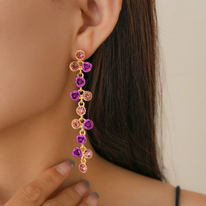 Détail de boucles d'oreilles pompons dorées avec roses violettes et strass roses
