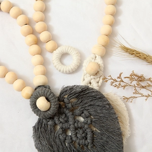 Detail of handmade cotton curtain tieback with natural wooden beads and grey leaf pendant