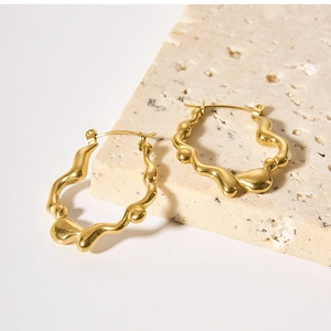 Detail of irregular wave-shaped 18K gold stainless steel earrings on stone surface