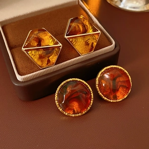 Macro detail of amber resin earrings with gold edges on a brown jewelry box texture