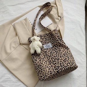Detailed shot of leopard print canvas tote with a plush bear charm on a beige blazer