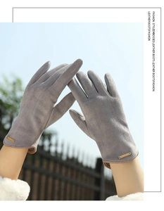 Close-up of grey suede gloves with brown leather edge and golden decorative nameplate