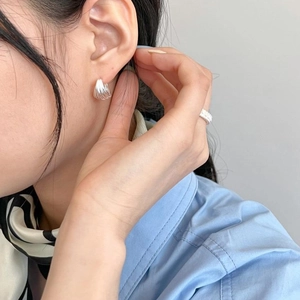 Detailed view of silver textured earrings with multi-layered folds and minimalist ring