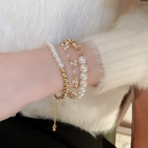 Detail of layered gold beaded bracelet set with white pearls on a model's wrist