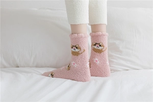 Close-up of thick pink coral fleece socks featuring cute cat jacquard on a white bed