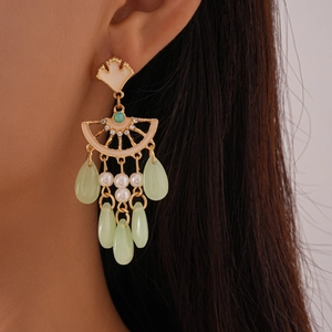 Détail de boucles d'oreilles feuille de ginkgo avec perles et pompons verts