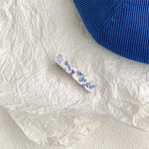 Detailed shot of blue and white marble pattern hair claw on white pleated paper background