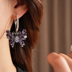 Close-up of a silver butterfly earring with purple zircon crystals worn by a model