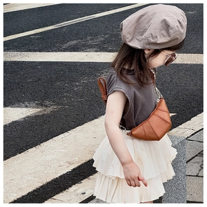 Side view of kid wearing a brown horn-shaped crossbody bag with a beige pleated skirt