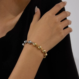 Détail d'un bracelet de perles minimaliste bicolore or et argent sur le poignet d'une femme