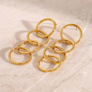 Macro detail of interlocking gold circles on long chain earrings against a stone background