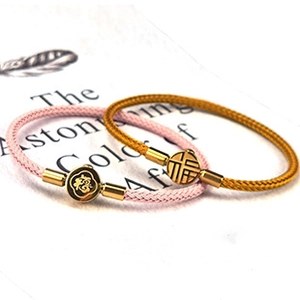 Dettaglio di braccialetti intrecciati rosa e oro con ciondoli tondi su sfondo libro