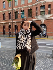 Outdoor shot of zebra striped knit scarf paired with a black tweed jacket and pleated skirt
