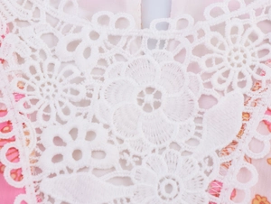Dettaglio dello scollo in pizzo bianco su tessuto in chiffon a fiori rosa
