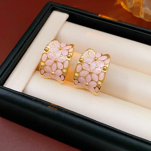 Détail de boucles d'oreilles fleurs en émail rose plaqué or dans un écrin