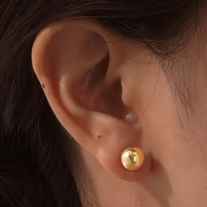 Close-up of a model wearing minimalist golden stainless steel ball earrings with mirror finish