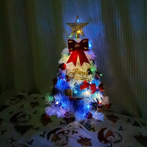 Close-up of mini white Christmas tree with blue LED lights and red bows on festive fabric