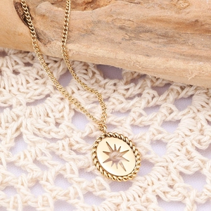 Close-up of golden oval pendant with sunburst cutout on a delicate chain over lace