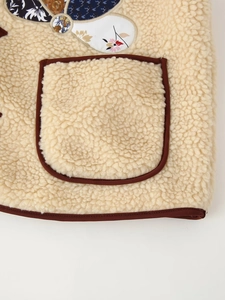 Close-up of beige faux shearling vest featuring brown trim and floral patch pockets