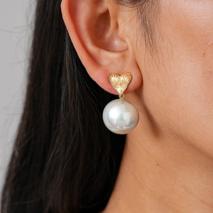 Detail of heart-shaped gold earring with textured finish and elegant white round pearl