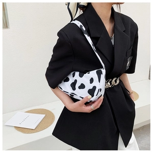 Side view of a trendy cow print shoulder bag worn by a model against a minimalist wall