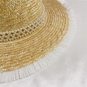 Close-up of straw hat featuring decorative white pearls and fringe trim details
