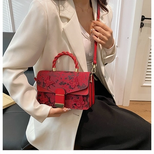 Fashionable red embroidered handbag with floral patterns held by a model in a white suit