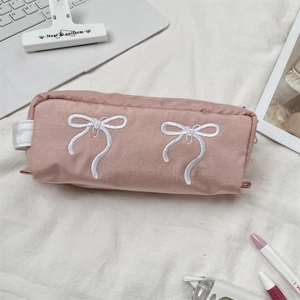 Dettaglio dell'astuccio in tela rosa con ricamo a fiocco bianco e manico laterale