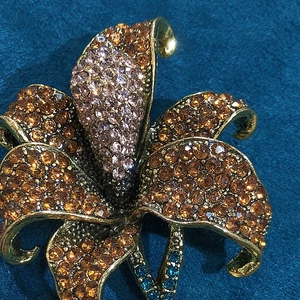 Macro detail of lily brooch with orange and purple rhinestones on golden alloy base