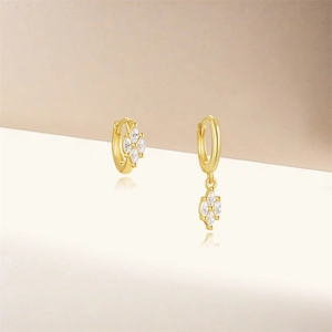 Macro shot of asymmetric gold earrings featuring marquise zircon petals and chain detail