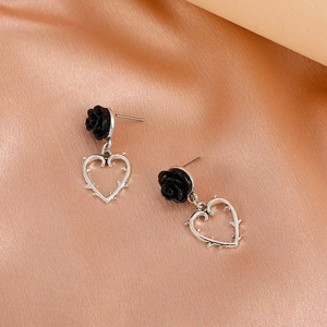 Close-up of gothic black rose heart earrings with silver thorn details on satin