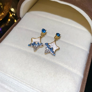 Macro shot of gold star drop earrings with blue crystals and white enamel inlay