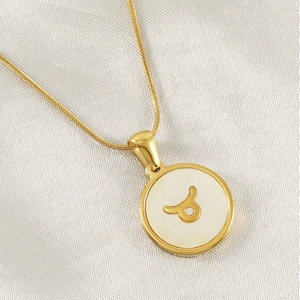 Macro view of gold 18K Taurus constellation pendant with white shell inlay on silk