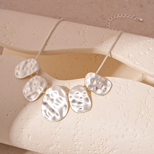 Detail of silver hammered irregular oval pendants on a textured beige display
