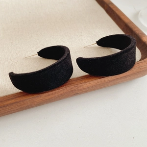 Close-up of black flocked C-shaped earrings on a wooden tray with linen padding