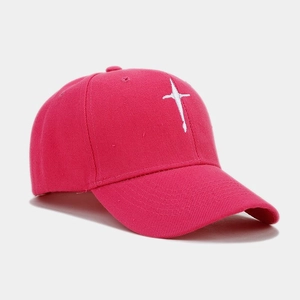 Close-up of white cross embroidery on a rose pink cotton twill baseball cap with stitching