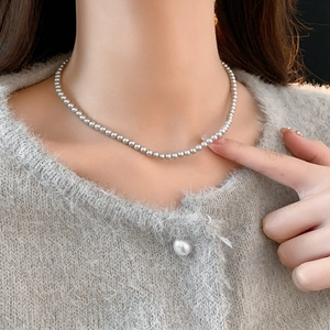 Close-up of minimalist pearl bead necklace worn on a soft grey knit sweater