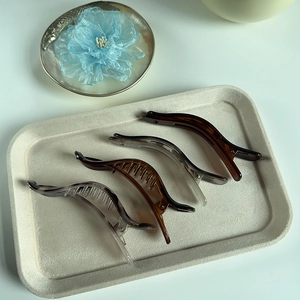 Set of four translucent matte curved duckbill hair clips on a beige textured tray