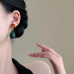 Close-up of asymmetrical water drop earrings with orange and green resin pendants
