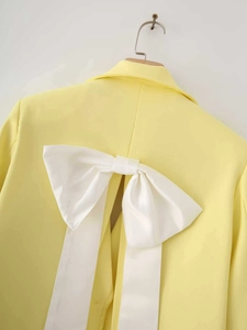 Detail view of yellow blazer back featuring a large white satin bow with split hem