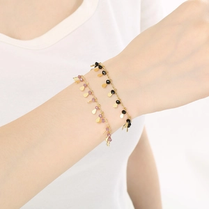 Elegant gold chain bracelet with purple and black beads and leaf charms on model wrist