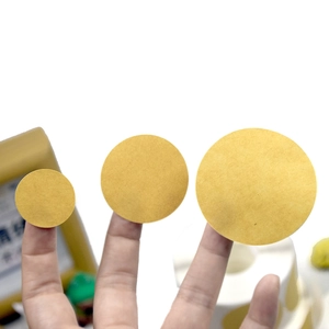 Three sizes of round gold adhesive labels shown on fingers for visual scale comparison