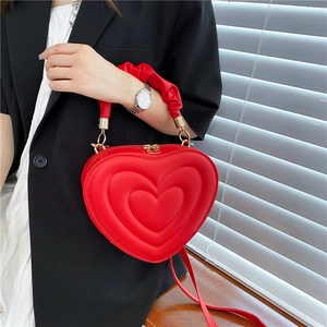 Red heart-shaped handbag with pleated handle and gold hardware on model