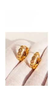 Detail view of gold hexagonal honeycomb hoop earrings with zircon stones on white glove