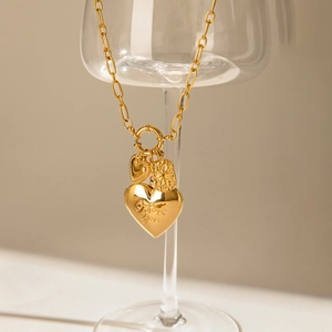 Gold stainless steel necklace with engraved heart pendants hanging on a glass cup