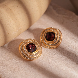Macro shot of vintage gold earrings with deep red stone and crystal halo on stone surface