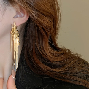 Detail of long gold tassel earrings with leaf-shaped charms worn by a model