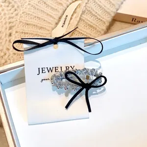 Pince à cheveux élégante avec perles argentées et nœud en velours noir sur carton