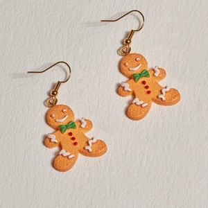Detailed view of gingerbread man earrings with green bowties and white icing detail