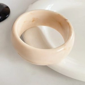 Macro detail of wide cream resin bangle with elegant marble texture on white ceramic